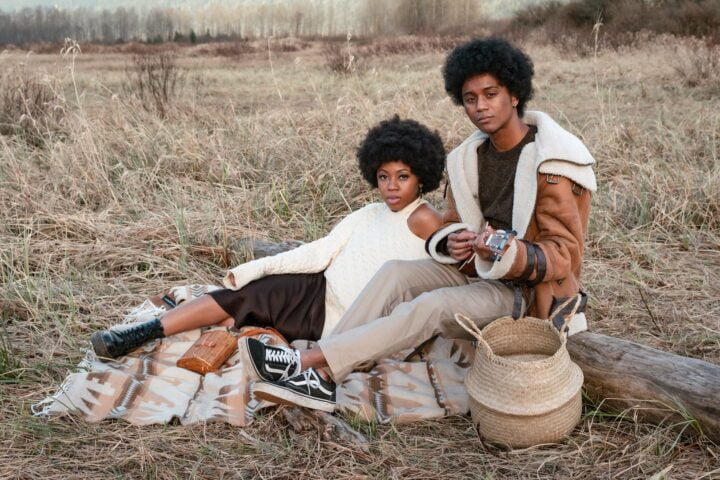 an afro haired man and woman sitting on a grassy field